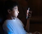 Un adolescent dans une pièce sombre, les yeux rivés sur un smartphone qui brille