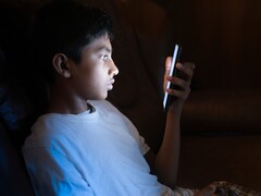 Un adolescent dans une pièce sombre, les yeux rivés sur un smartphone qui brille