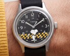 Gros plan sur le cadran noir de la Timex MK1 représentant Snoopy sur un fond à carreaux jaunes et noirs, avec des index arabes et des aiguilles luminescentes.