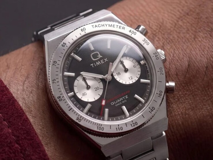 La montre Timex Q Timex Continental Chronograph TW2Y93200 au poignet, dotée d’un cadran noir radial de style CD, de deux sous-cadrans argentés, d’une lunette tachymétrique, d’index luminescents et d’un bracelet intégré en acier inoxydable.