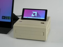 Un mini PC Ayaneo AM01S de style rétro en finition beige, doté d'un écran secondaire rabattable intégré affichant le bureau Windows. (ETA Prime via YouTube)