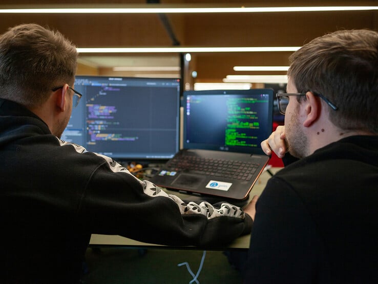 Des chercheurs analysent du code sur deux écrans (Image source : Flipsnack / Unsplash)