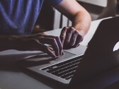 Des mains tapant sur le clavier d’un MacBook dans la pénombre, le logo Apple illuminé