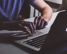 Des mains tapant sur le clavier d’un MacBook dans la pénombre, le logo Apple illuminé