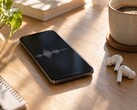 Smartphone affichant une forme d’onde audio à côté d’écouteurs sans fil et d’une tasse de café sur un bureau en bois