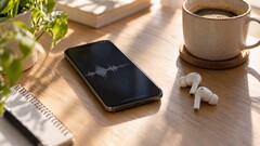 Smartphone affichant une forme d’onde audio à côté d’écouteurs sans fil et d’une tasse de café sur un bureau en bois