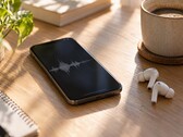 Smartphone affichant une forme d’onde audio à côté d’écouteurs sans fil et d’une tasse de café sur un bureau en bois