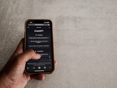 Main tenant un smartphone affichant l’interface de ChatGPT au-dessus d’une surface en pierre grise