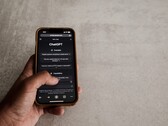 Main tenant un smartphone affichant l’interface de ChatGPT au-dessus d’une surface en pierre grise