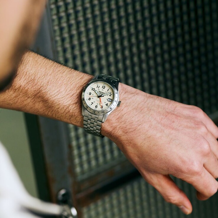 Vue de face de la Seiko 5 Sports Field GMT HDB002, dotée d'un cadran crème, d'une aiguille GMT orange, d'une lunette fixe de 24 heures et d'un bracelet en acier inoxydable.
