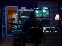 Un chercheur cagoulé travaille sur plusieurs écrans dans une installation sombre. Photo d'un pirate générique. 