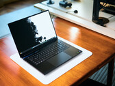 Un ordinateur portable de jeu Razer Blade 16 noir mat, ouvert, posé sur un tapis de bureau blanc posé à son tour sur une table en bois aux teintes chaudes, affichant un fond d'écran en noir et blanc aux couleurs vives.