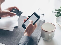 Personne tapotant sur un smartphone tout en tenant une carte bancaire dans l'autre main
