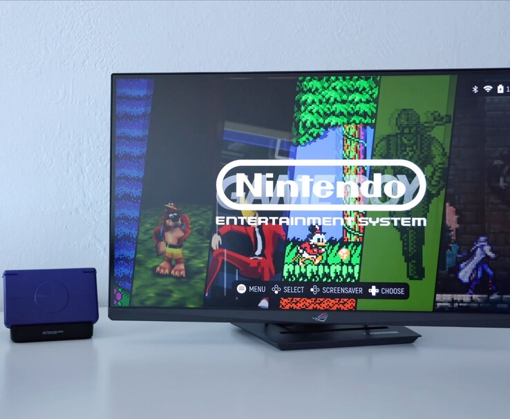 Retroid Pocket Flip 2 en violet placé sur une station d'accueil à côté d'un moniteur, l'écran de télévision affichant l'interface d'un émulateur NES rétro. (Source de l'image : Retro Game Corps sur YouTube)