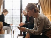 Une adolescente regarde son smartphone, tandis que deux adultes sont assis, flous, à l’arrière-plan.