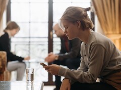 Une adolescente regarde son smartphone, tandis que deux adultes sont assis, flous, à l’arrière-plan.