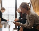 Une adolescente regarde son smartphone, tandis que deux adultes sont assis, flous, à l’arrière-plan.