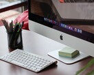 Un iMac posé sur un bureau, avec le dock macOS visible à l'écran et un clavier Apple devant