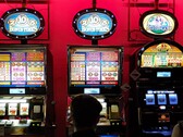 Machines à sous à l'intérieur d'un casino avec des écrans lumineux et des personnes jouant devant (Image source : djedj via Pixabay)