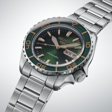 Gros plan de la Seiko 5 Sports SKX HDB005, mettant en valeur son cadran vert foncé, ses aiguilles couleur or rose et ses index appliqués, ainsi que sa lunette verte assortie aux graduations dorées.