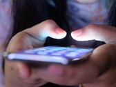 Deux mains tiennent un smartphone à l’écran lumineux dans la pénombre