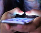 Deux mains tiennent un smartphone à l’écran lumineux dans la pénombre