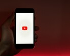 Une main tenant un smartphone dont l'écran affiche le logo YouTube, sur fond rouge