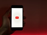Une main tenant un smartphone dont l'écran affiche le logo YouTube, sur fond rouge
