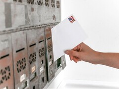 Une main déposant une enveloppe dans une rangée de boîtes aux lettres