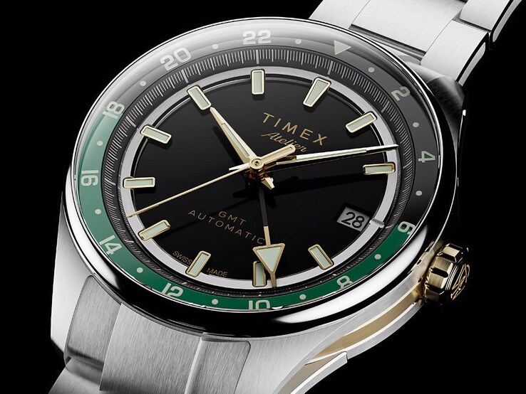 Vue de biais de la Timex Atelier GMT Première M1a, montrant son cadran noir, son anneau GMT vert, sa couronne dorée et son bracelet en acier inoxydable.