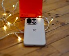 Un OnePlus 15 repose sur une table en bois, entouré de guirlandes lumineuses aux couleurs chaudes, avec un coffret de vente OnePlus rouge vif placé en arrière-plan.