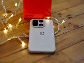 Un OnePlus 15 repose sur une table en bois, entouré de guirlandes lumineuses aux couleurs chaudes, avec un coffret de vente OnePlus rouge vif placé en arrière-plan.