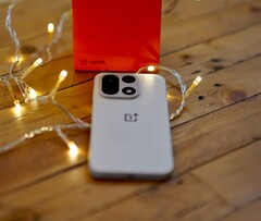 Un OnePlus 15 repose sur une table en bois, entouré de guirlandes lumineuses aux couleurs chaudes, avec un coffret de vente OnePlus rouge vif placé en arrière-plan.