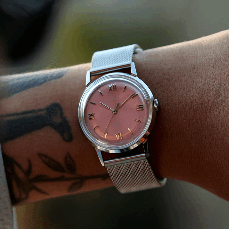 Personne portant la montre Timex x Todd Snyder Marlin Mesh, dotée d’un cadran saumon à effet soleil et d’un bracelet en maille.