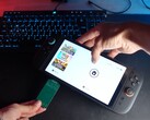 Yu de la chaîne YouTube Better Gaming tenant une Nintendo Switch 2 dans une main et un adaptateur PCB vert open-source dans l'autre, tentant de l'insérer dans l'emplacement microSD Express de l'appareil (Source d'image : Better Gaming via YouTube)