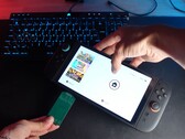 Yu de la chaîne YouTube Better Gaming tenant une Nintendo Switch 2 dans une main et un adaptateur PCB vert open-source dans l'autre, tentant de l'insérer dans l'emplacement microSD Express de l'appareil (Source d'image : Better Gaming via YouTube)