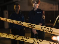 Deux policiers se tenant debout la nuit derrière un ruban jaune portant l’inscription Stop