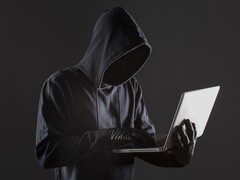 Un pirate informatique cagoulé utilisant un ordinateur portable sur un fond sombre.