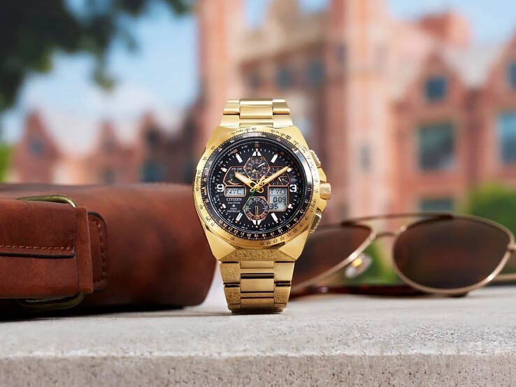 Montre de pilote Citizen Promaster Skyhawk A-T JY8144-50E de couleur dorée, posée à la verticale sur un rebord à côté d’un sac en cuir marron et de lunettes de soleil, avec un paysage urbain flou en arrière-plan.