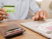 Personne tenant une carte bancaire devant un ordinateur portable, avec un portefeuille sur le bureau