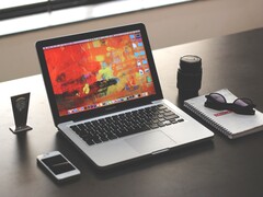 MacBook Pro posé sur un bureau sombre, à côté d’un smartphone, de lunettes et d’un carnet