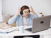 Homme portant un casque et levant les mains de frustration devant un ordinateur portable