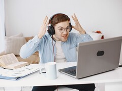 Homme portant un casque et levant les mains de frustration devant un ordinateur portable