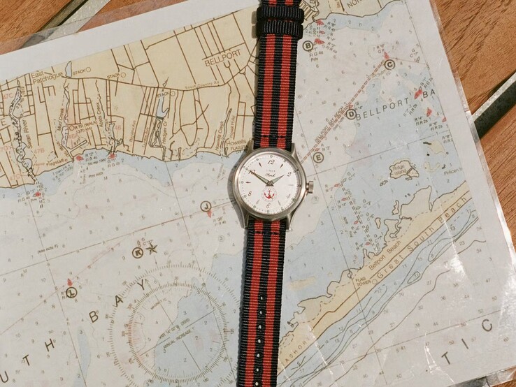 Montre Noah x Timex MK1 Anchor, dotée d’un bracelet en tissu rayé bleu marine et rouge, posée sur une carte marine.