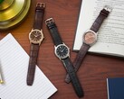 Trois montres Citizen Rolan disposées sur un bureau en bois, à côté d'un cahier, d'un stylo, d'une lampe et d'un livre ouvert, dont le modèle AW2110-14Z au cadran saumon.
