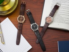Trois montres Citizen Rolan disposées sur un bureau en bois, à côté d'un cahier, d'un stylo, d'une lampe et d'un livre ouvert, dont le modèle AW2110-14Z au cadran saumon.