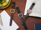 Trois montres Citizen Rolan disposées sur un bureau en bois, à côté d'un cahier, d'un stylo, d'une lampe et d'un livre ouvert, dont le modèle AW2110-14Z au cadran saumon.