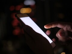 Une main tenant un smartphone dont l'écran brille dans l'obscurité
