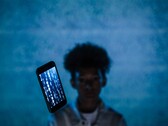 Smartphone flottant avec du code sur son écran devant un fond bleu, avec une personne floue derrière lui