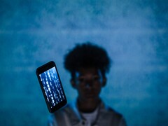 Smartphone flottant avec du code sur son écran devant un fond bleu, avec une personne floue derrière lui